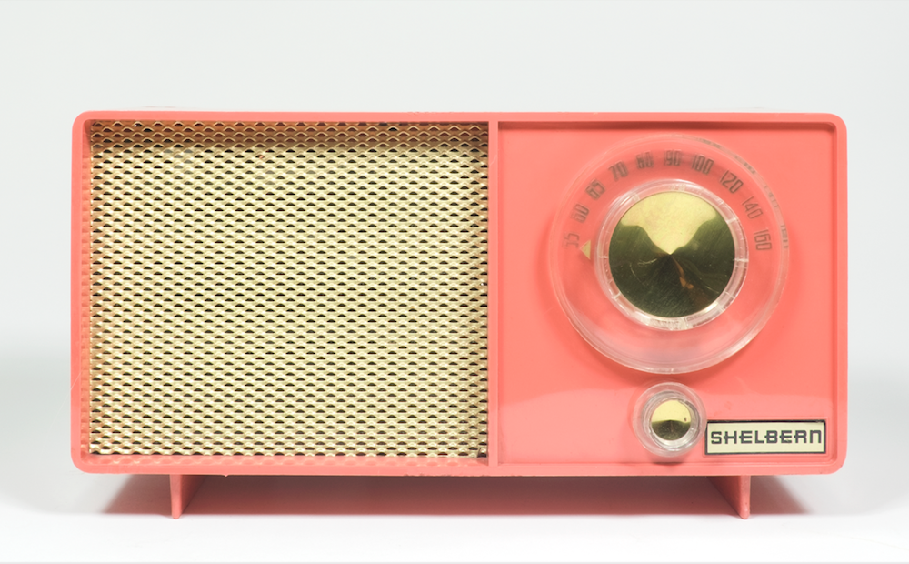 This bright pink plastic tube radio has an eggshell-coloured speaker grill on the left side, and a golden-coloured dial on the right.