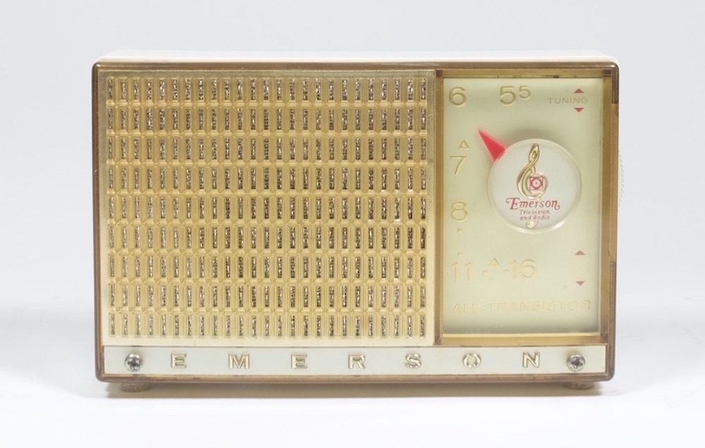 Une petite radio carrée de couleur dorée avec un cadran à droite. L'aiguille du cadran en forme de flèche est rouge vif.