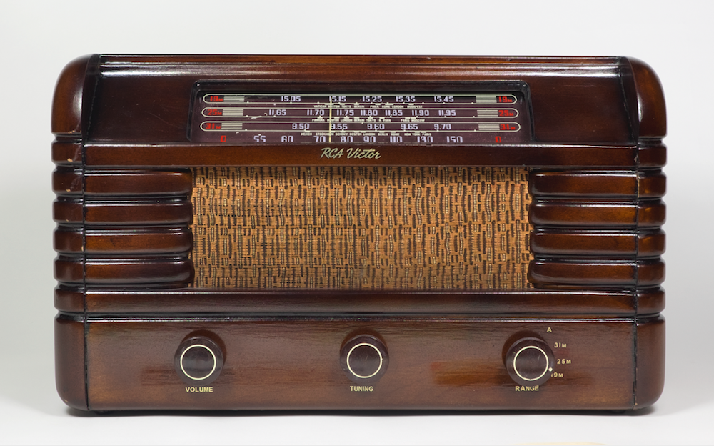 La radio est contenue dans un meuble en bois strié avec des cadrans sur le devant et un affichage sur le bord supérieur.