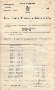 Front side of a signed radio licence bearing the coat of Canada and a list of frequency numbers with the French word temporaire typed in red ink. The text is in French.
