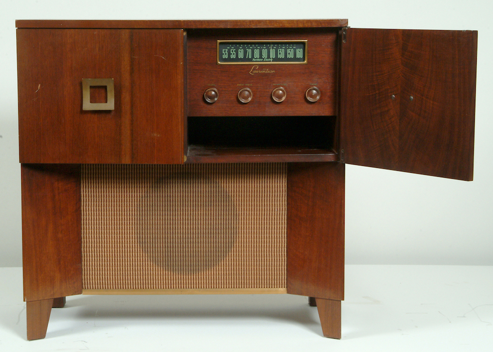The radio is housed in a large wooden cabinet and shown with its right door open. The large speaker takes up the lower half. Theradio dial takes the space on the front right corner.