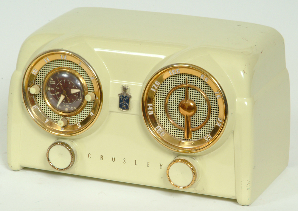 The horizontally oriented cream-white radio has two round dials with brass finishing that hide the perforated openings of the speakers. Two knobs are below each dial.