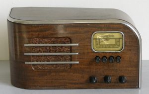 Housed in wood laminate with horizontal metal trims. The radio has a horizontally rounded front edge on the left side and a vertically rounded top edge on the right side.