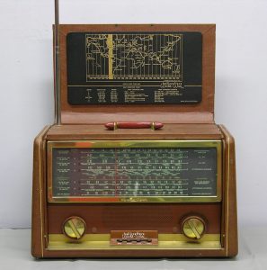 This brown wood radio flips open with the front panel displayed above the radio like a board. When opened, you see the large, black dial window with golden knobs below.