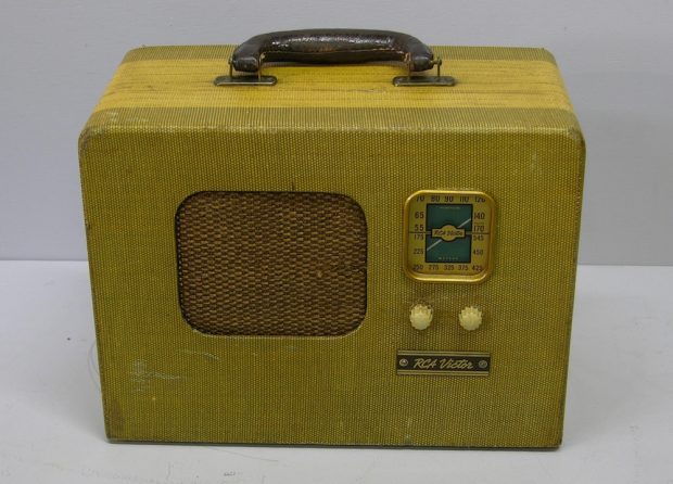 Shaped like a rectangle with a handle on the top, a speaker in the middle, two dials on the side, with a display on top. The radio has a yellow-green cloth finish.