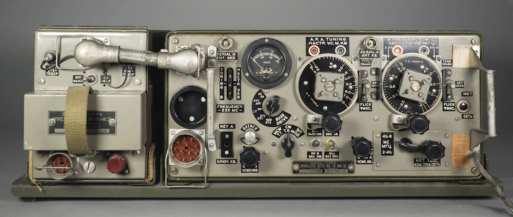 This radio transceiver is a low rectangular model made of metal with many knobs and dials. The labeling is in English and Russian.