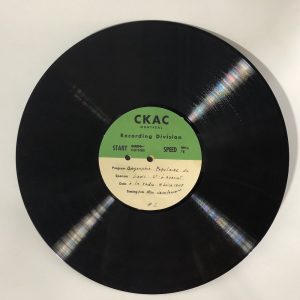 A twelve-inch transcription record with a green and white paper label and black print and black handwriting to document the recorded content.