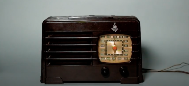 Plastic tabletop radio with horizontal grille on left and rounded square dial on right. Two switches below the dial.