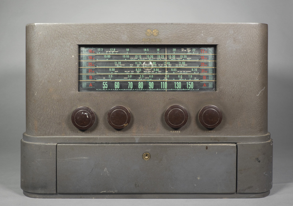 This table top radio has a grey painted exterior with curved edges and no further decoration. At the bottom is a lockable drawer.