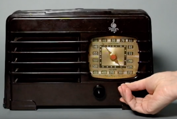 1940 Emerson radio with a hand turning a dial below a brass coloured frequency display window.