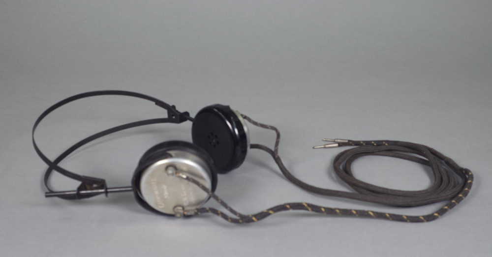 A set of headphones with black earpieces and a two-prong input at the end of the cotton covered cable.