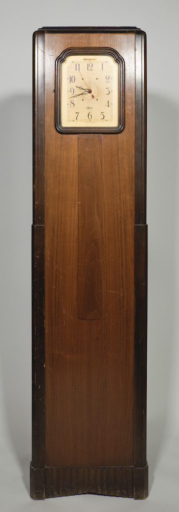 A warm-coloured wood casing holds this radio, while only the clock dial is visible in the top part of this tall furniture piece.