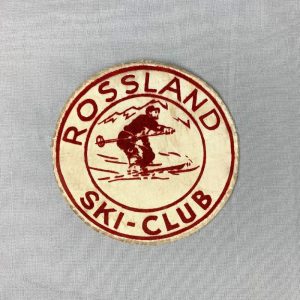 Round, beige patch with red lettering and a graphic of a skier in the centre.