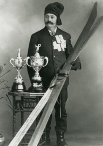 Olaus Jeldness posing with a pair of skis and two ski trophies.