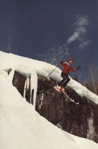Young skier mid-air after jumping off a cliff on a snowy mountain.