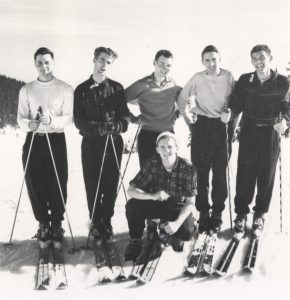 Six men on skis posing for a photograph on a snowy mountain.