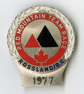 Silver pin with red and black detailing which says Red Mountain Team Race Rossland B.C. 1977.