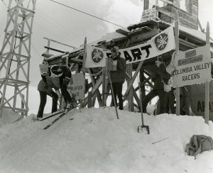 Black and white photograph of a skier pushing off from a starting gate.