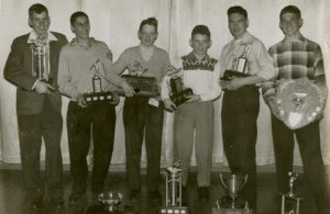 Six young men holding trophies. There are also four more trophies on the ground in front of the group.