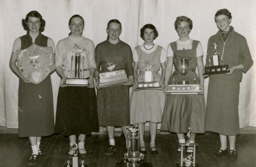 Six young women holding trophies. There are also three more trophies on the ground in front of the group.