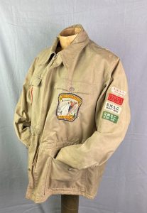 A beige jacket with various colourful patches on the chest and proper left sleeve.