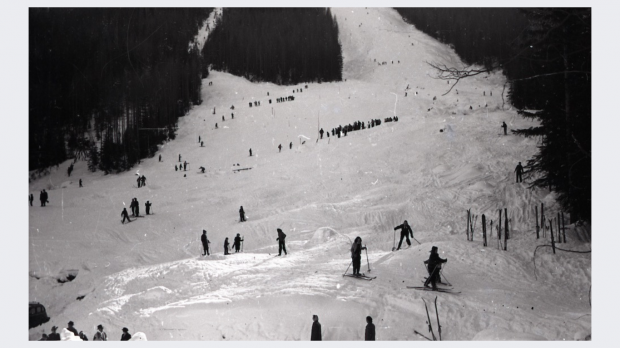 Black and white photo of ski hill and skiers taken looking up Red Mountain.