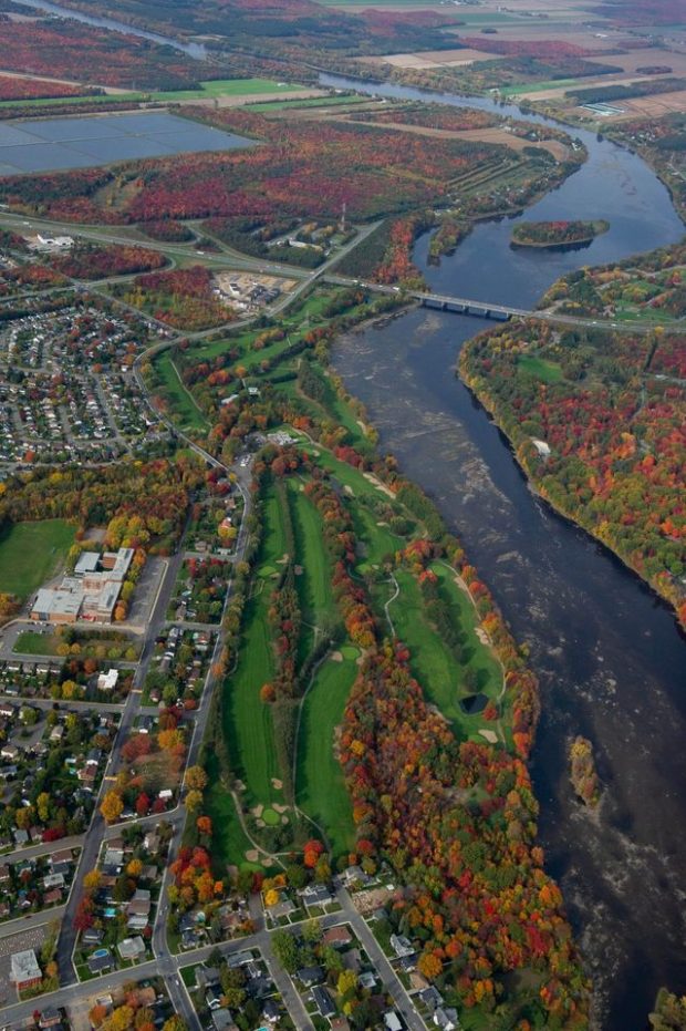 Colour photograph showing an aerial view of the golf course in the autumn, along the Saint Francis River. It also shows the development of the city and the landscaping around the golf course.