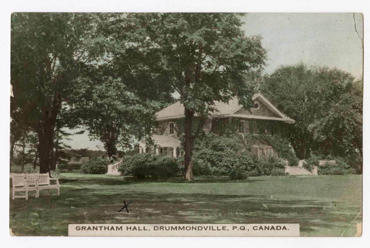 Photographie en noir et blanc du Grantham Hall, une grande maison en pierre de deux étages couverte de plantes grimpantes avec de grands escaliers donnant sur les jardins de la propriété. Les jardins sont constitués d’arbustes et d’arbres matures.