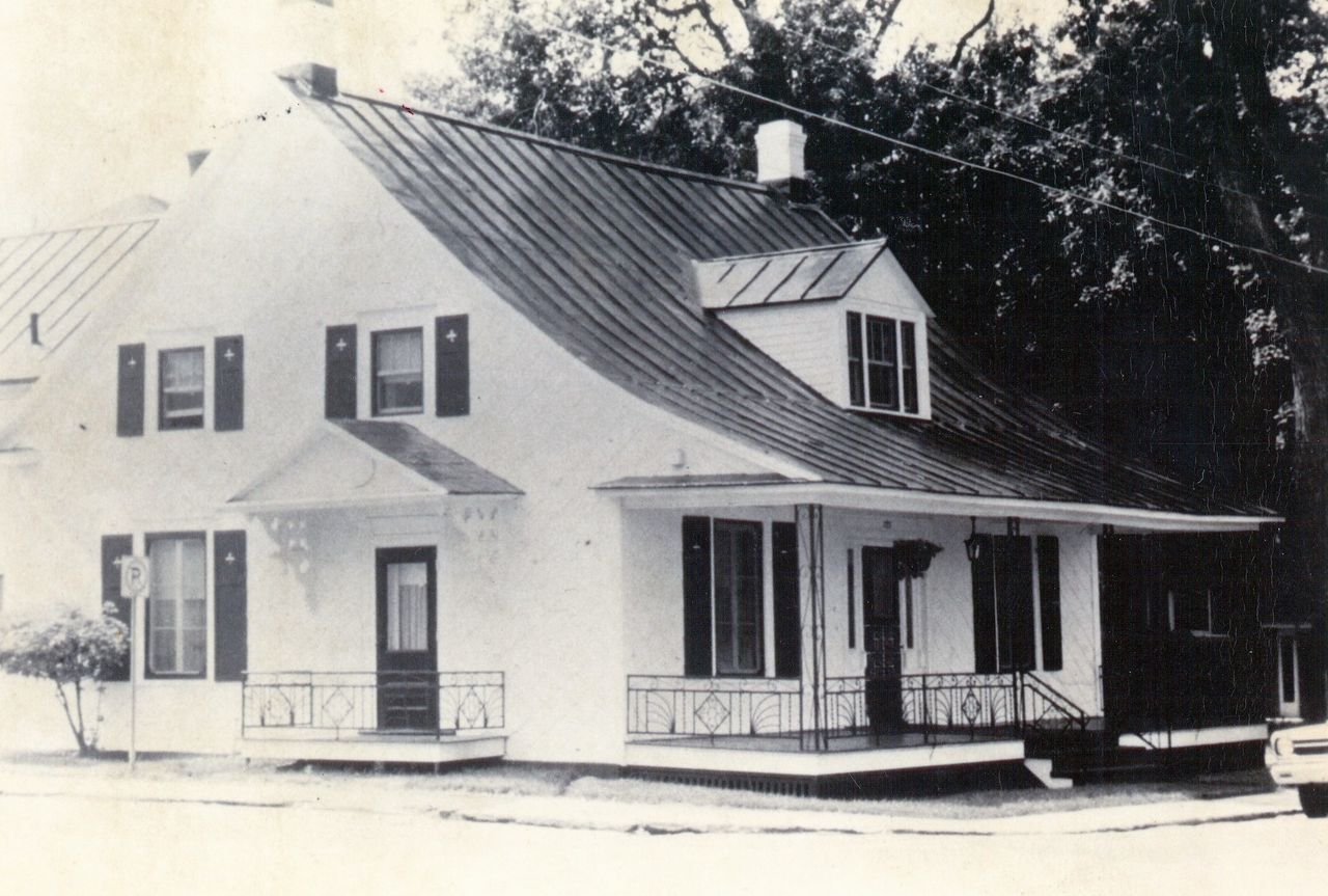 Black and white photograph of a Quebec-style house with shutters around the windows and a cast iron railing around the porch.