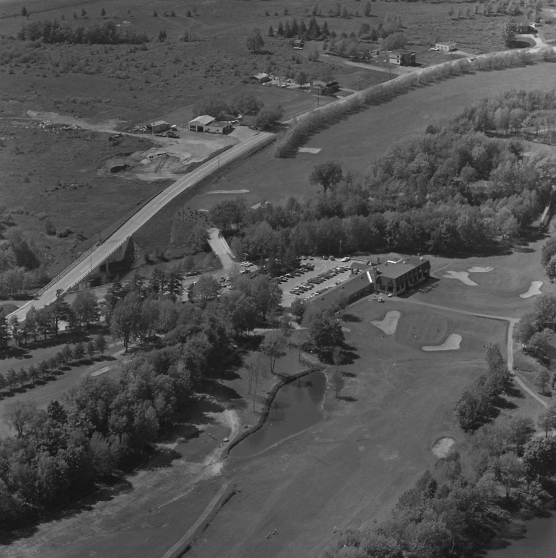 Photographie en noir et blanc démontrant une vue aérienne du terrain de golf. On y voit le chalet principal et plusieurs trappes de sable sur le parcours.