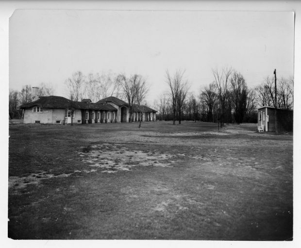 Black and white photograph of the Drummondville Golf & Country Club clubhouse. The building, which is built lengthwise, is covered in climbing plants and surrounded by trees.