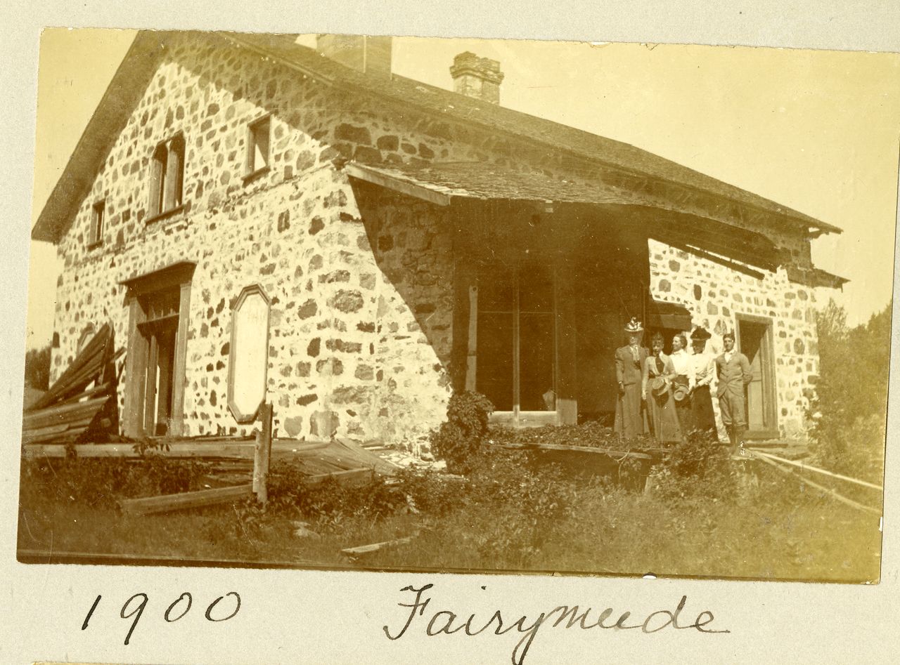 Black and white photograph of a stone house with several arched windows and family members posing in front of the house.