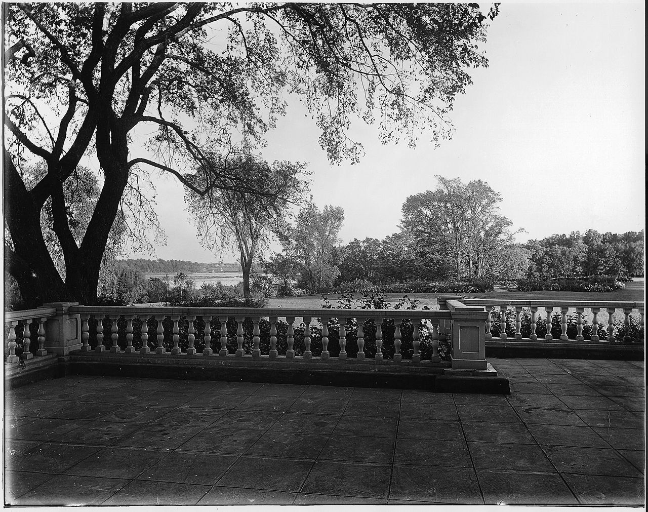Black and white photograph of a view from the stone porch of Grantham Hall. Vegetation can be seen on the right, and the Saint Francis River and the railway bridge crossing it on the left.