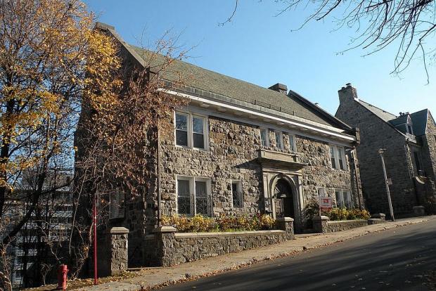 Colour photograph of a colonial-style stone house surrounded by a stone wall.