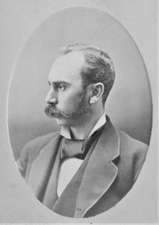 Black and white photograph of a man posing in profile, wearing a jacket and a scarf.