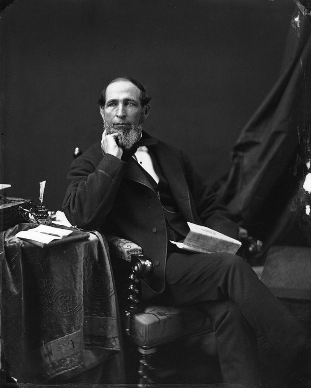 Black and white photograph of a man sitting in a chair and holding a newspaper.