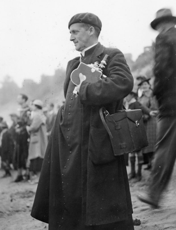 Albert Tessier stands, camera in hand, on a beach among other spectators of the canoe race.