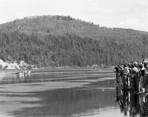 On the banks, spectators get as close to the water as possible to see the passing canoeists, who seem so tiny in the middle of the wide river and high cliffs.