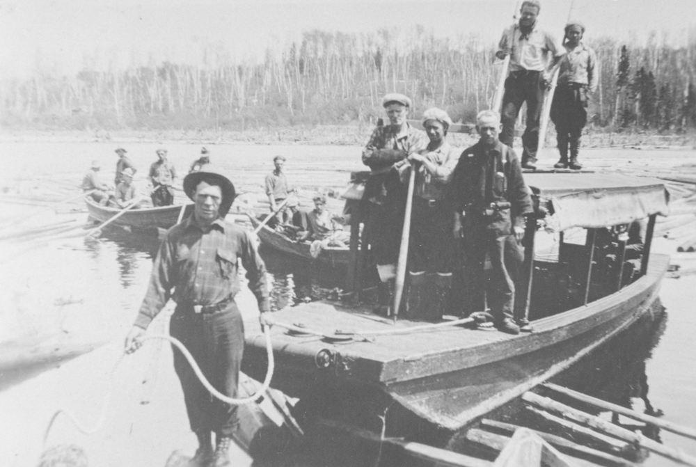 Plusieurs hommes se tiennent dans des embarcations sur une rivière où flottent plusieurs billots de bois.