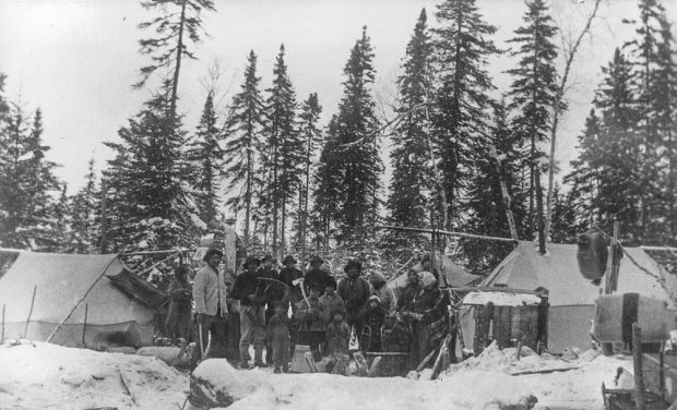 Indigenous people of all ages pose in the snow amidst rudimentary tents in the forest