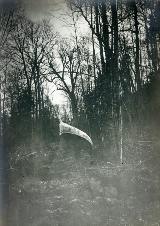 A man carries a canoe on his shoulders in the middle of the forest.