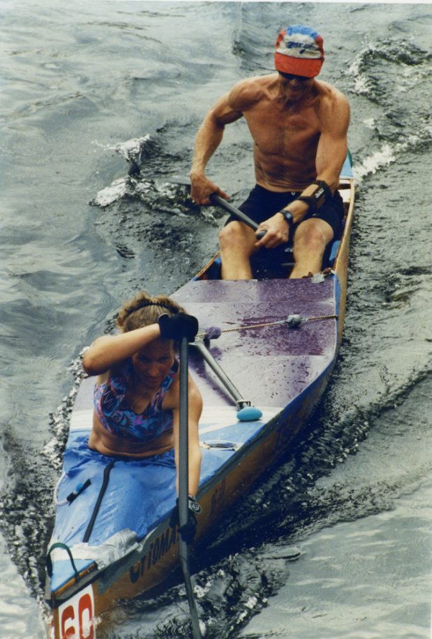 A man and a woman sit in a canoe, both rowing hard.