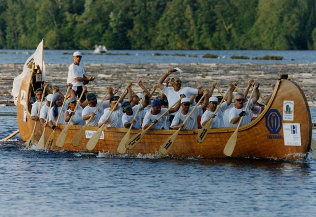 20 men and women are rowing to move a large rabaska forward.
