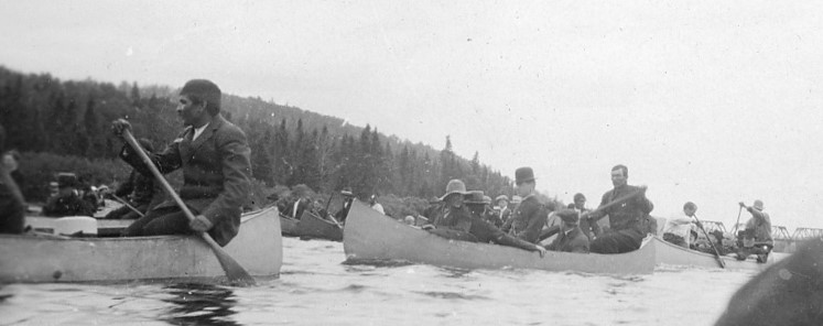 Indigenous people are sitting in canoes filled with belongings on the river.