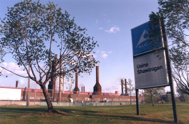 The foreground is occupied by a sign that says: Alan, Usine Shawinigan (Alan, Shawinigan Plant). In the background, behind a fence, the factory and its chimneys dominate the landscape.