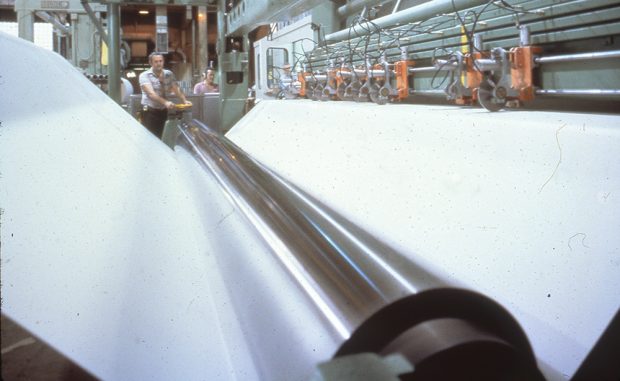 A man watches a huge sheet of paper pass through a roller