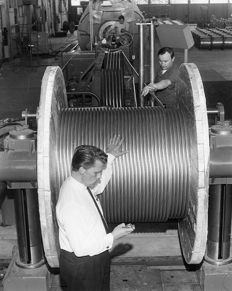 Des employés surveillent l'enroulement d'un large câble d'aluminium sur une grande bobine de bois.