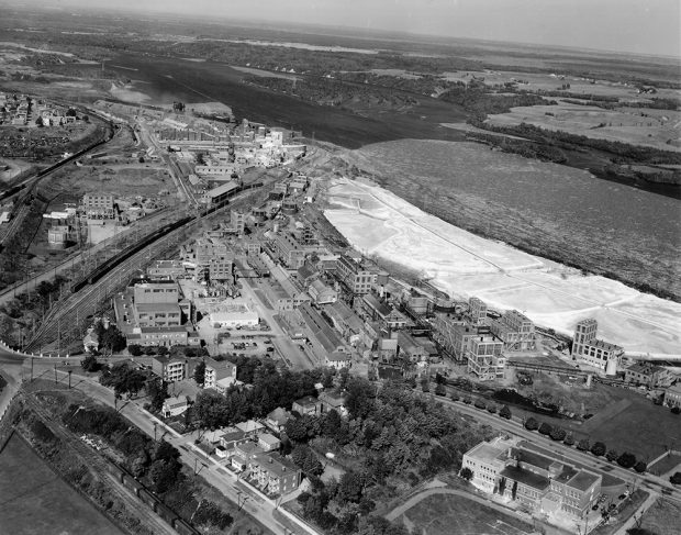 Aerial view of the vast mill site that stretches near the river on which floats both thousands of logs and a whitish lime residue.