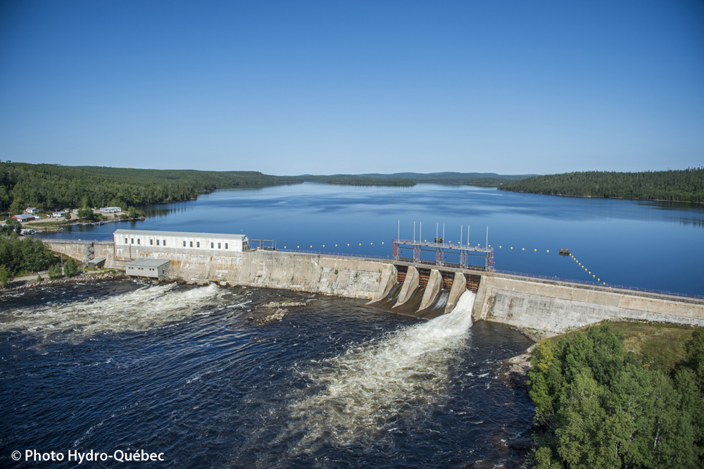 La structure de béton du barrage Gouin se déploie sur la largeur de la rivière. Le réservoir Gouin s’étend derrière le barrage.