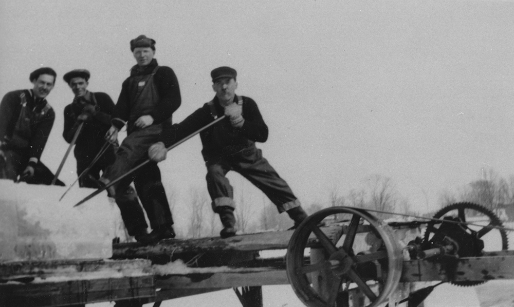 Black and white photograph of four ice cutters loading a trailer with huge blocks of ice.